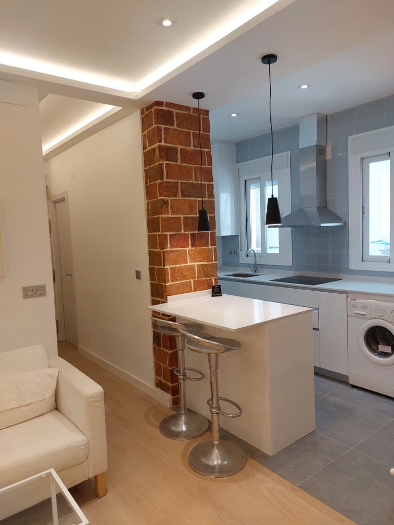 Cocina semiabierta con barra americana y pared de ladrillo visto en una reforma en Madrid